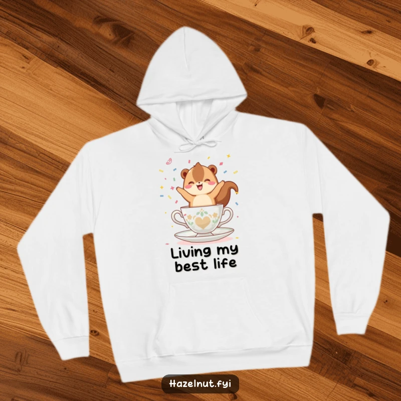 Funny, happy hazelnut balancing on a teacup, throwing confetti, featured on a cozy hoodie, perfect for warm and festive occasions.